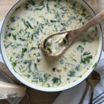 Italian chicken gnocchi soup in a white Dutch oven with creamy broth, shredded chicken, gnocchi, and baby kale, styled on a wooden board with a wooden spoon.