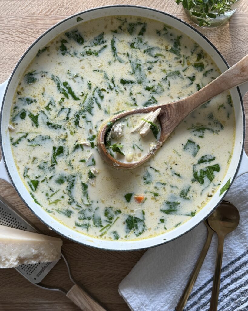 Italian chicken gnocchi soup in a white Dutch oven with creamy broth, shredded chicken, gnocchi, and baby kale, styled on a wooden board with a wooden spoon.