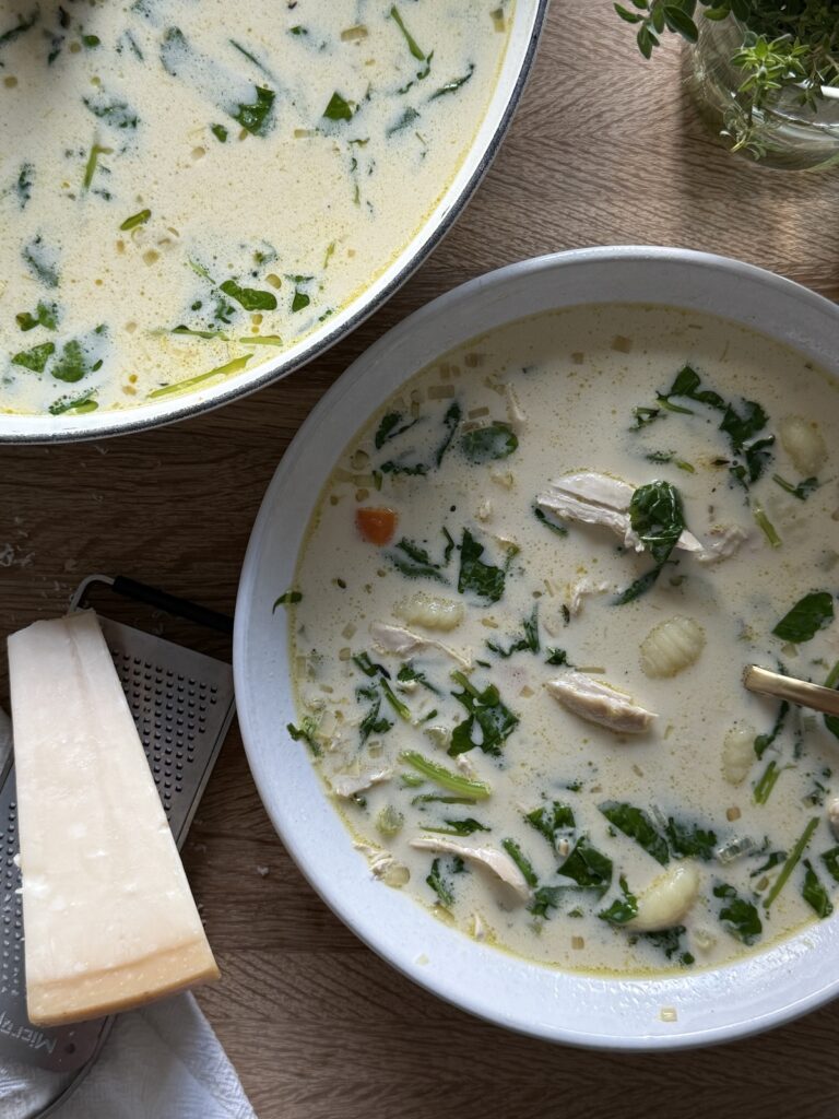 Italian chicken gnocchi soup in a white bowl with gnocchi, shredded chicken, spinach, and creamy broth on a wooden cutting board