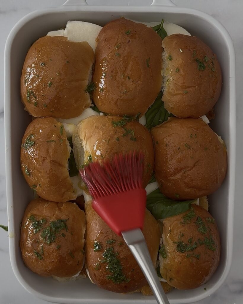 Brushing slider buns with garlic-parsley olive oil for chicken parm sliders before baking