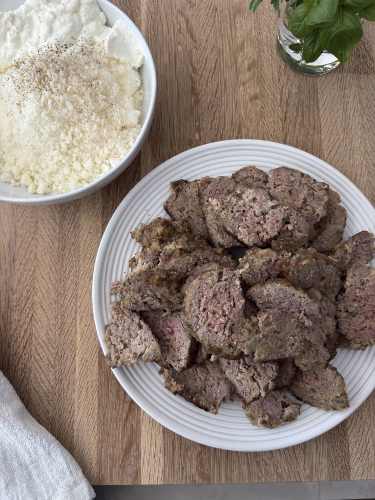 Baked ricotta meatballs sliced on a plate with ricotta and Parmesan, ready to layer into homemade meatball lasagna.