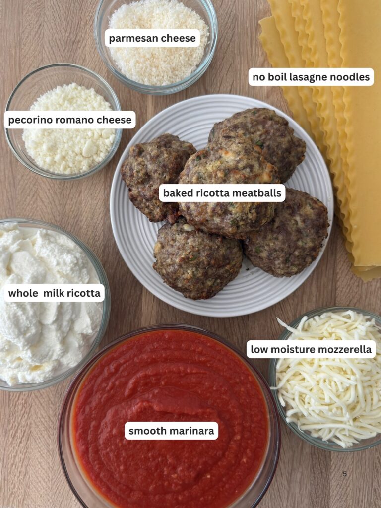 Overhead view of meatball lasagna ingredients, including baked ricotta meatballs, no-boil lasagna noodles, smooth marinara sauce, ricotta, Parmesan, Pecorino Romano, and shredded mozzarella.