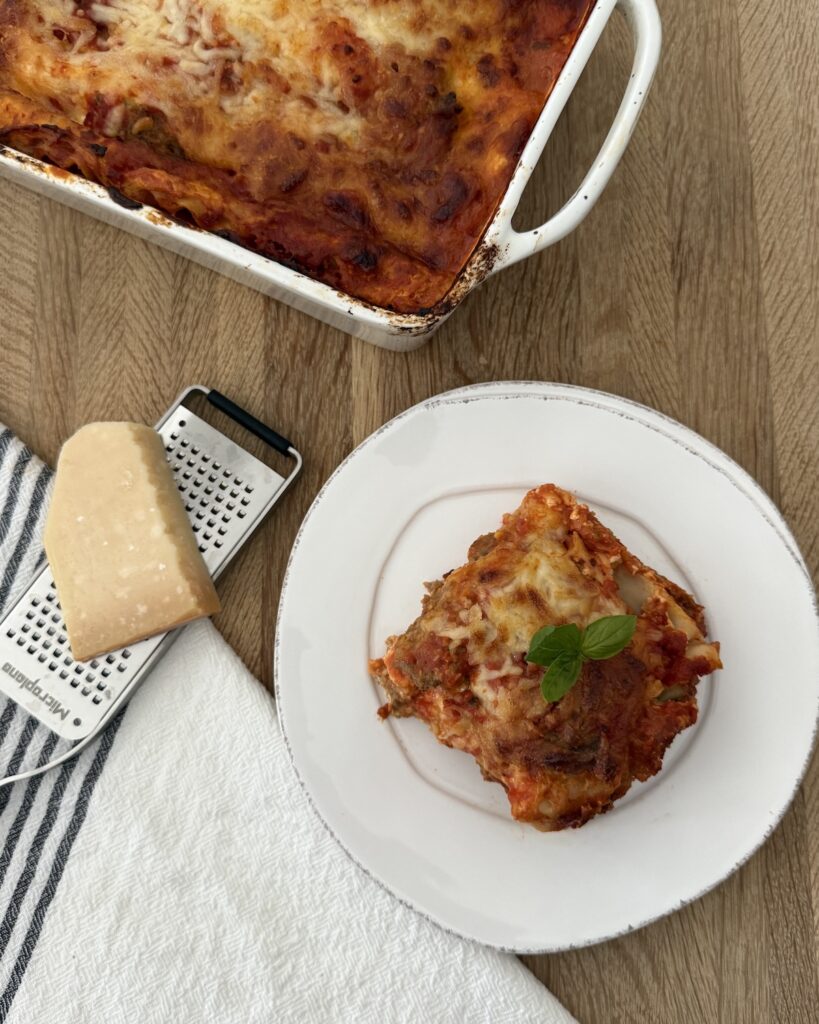 Homemade meatball lasagna baked in a pan with a slice served on marinara sauce and a wedge of Parmesan cheese on the side.
