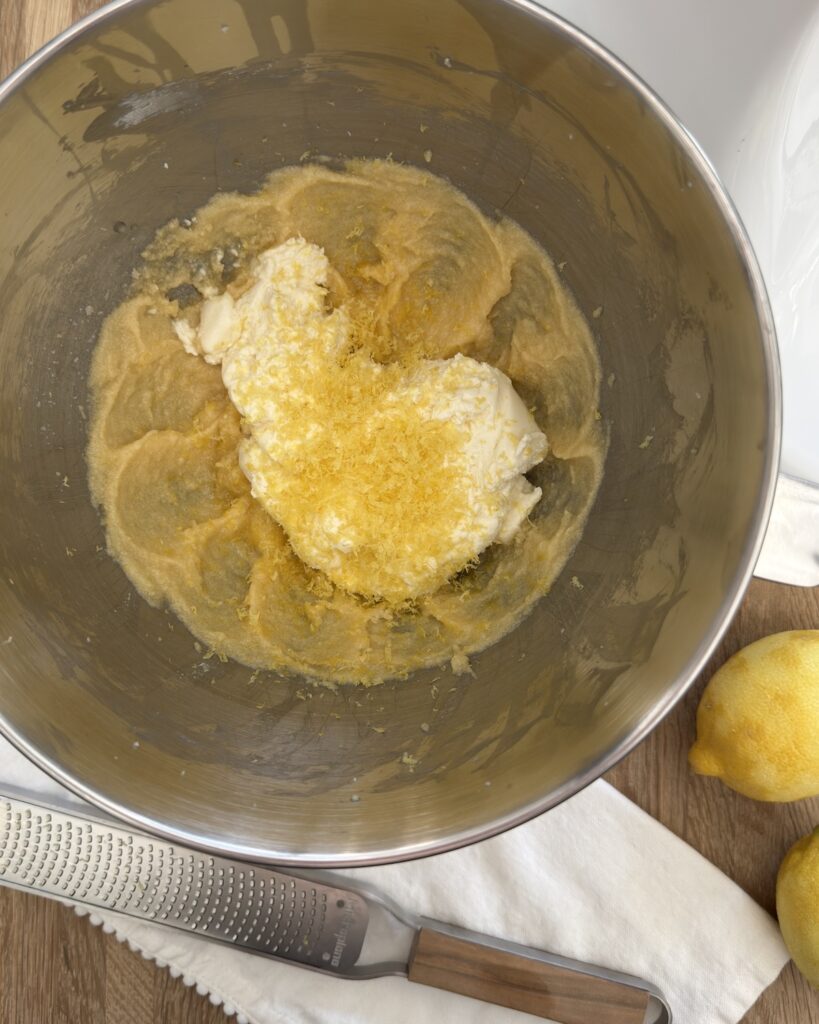 Lemon ricotta cookie dough in a mixing bowl with drained ricotta and fresh lemon zest added to creamed butter, sugar, and eggs.