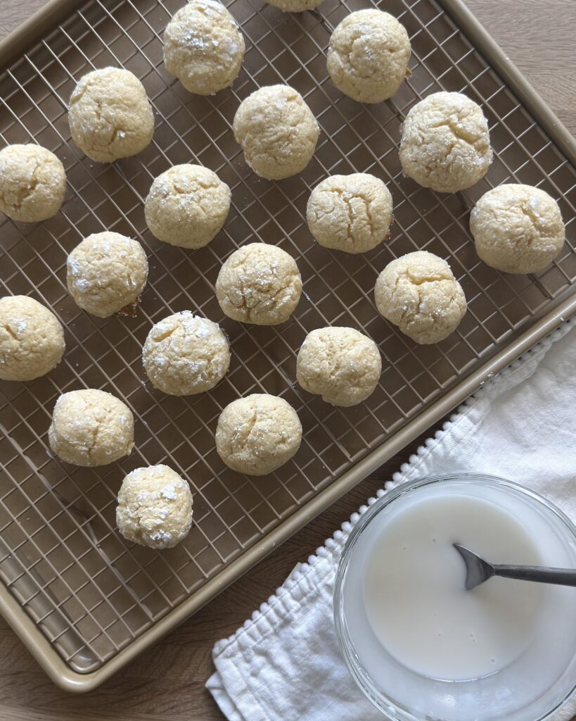 Lemon ricotta cookies cooling on a wire rack with a bowl of lemon glaze ready for glazing.