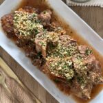 Slow cooker osso buco arranged on a serving platter with braising sauce and topped with breadcrumb gremolata, with extra gremolata in a small bowl on the side.