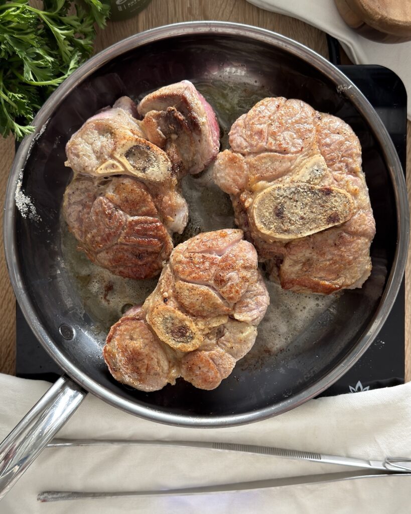 Seared veal shanks for slow cooker osso buco browning in a stainless steel skillet.