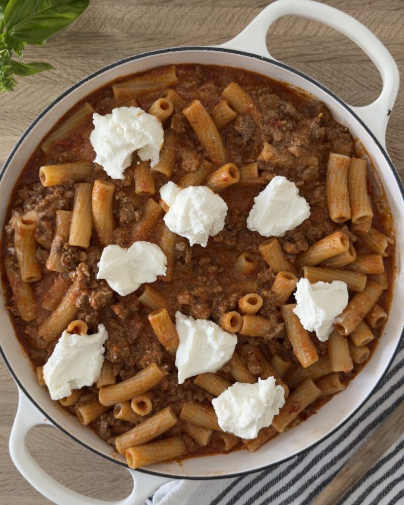 Overhead view of baked bolognese pasta in a white Dutch oven with dollops of ricotta cheese on top