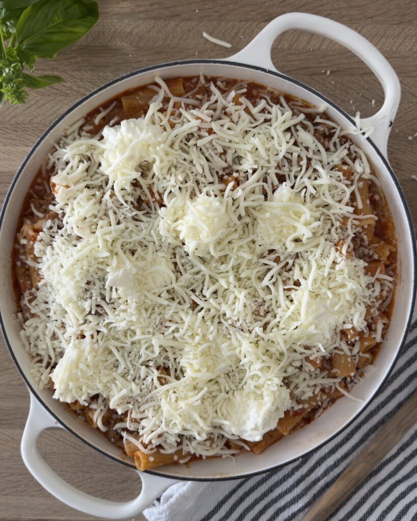 Overhead view of baked bolognese pasta in a white Dutch oven topped with mozzarella and dollops of ricotta cheese