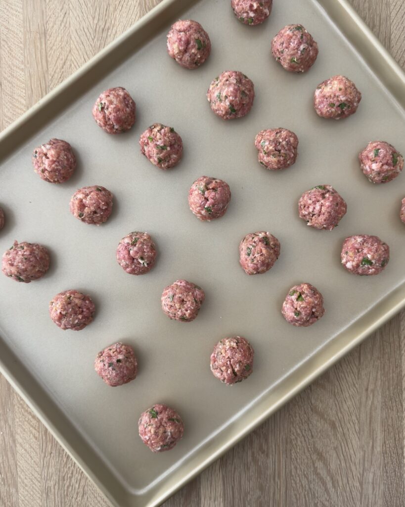 Homemade Italian wedding soup meatballs arranged on a baking sheet, made with seasoned ground meat and herbs before cooking.