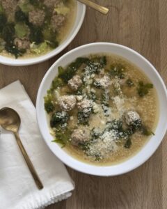 Italian wedding soup with homemade meatballs, acini di pepe pasta, and rich broth, topped with grated Parmesan cheese in a white bowl on a wooden table.