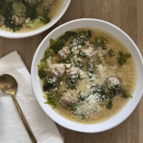Italian wedding soup with homemade meatballs, acini di pepe pasta, and rich broth, topped with grated Parmesan cheese in a white bowl on a wooden table.