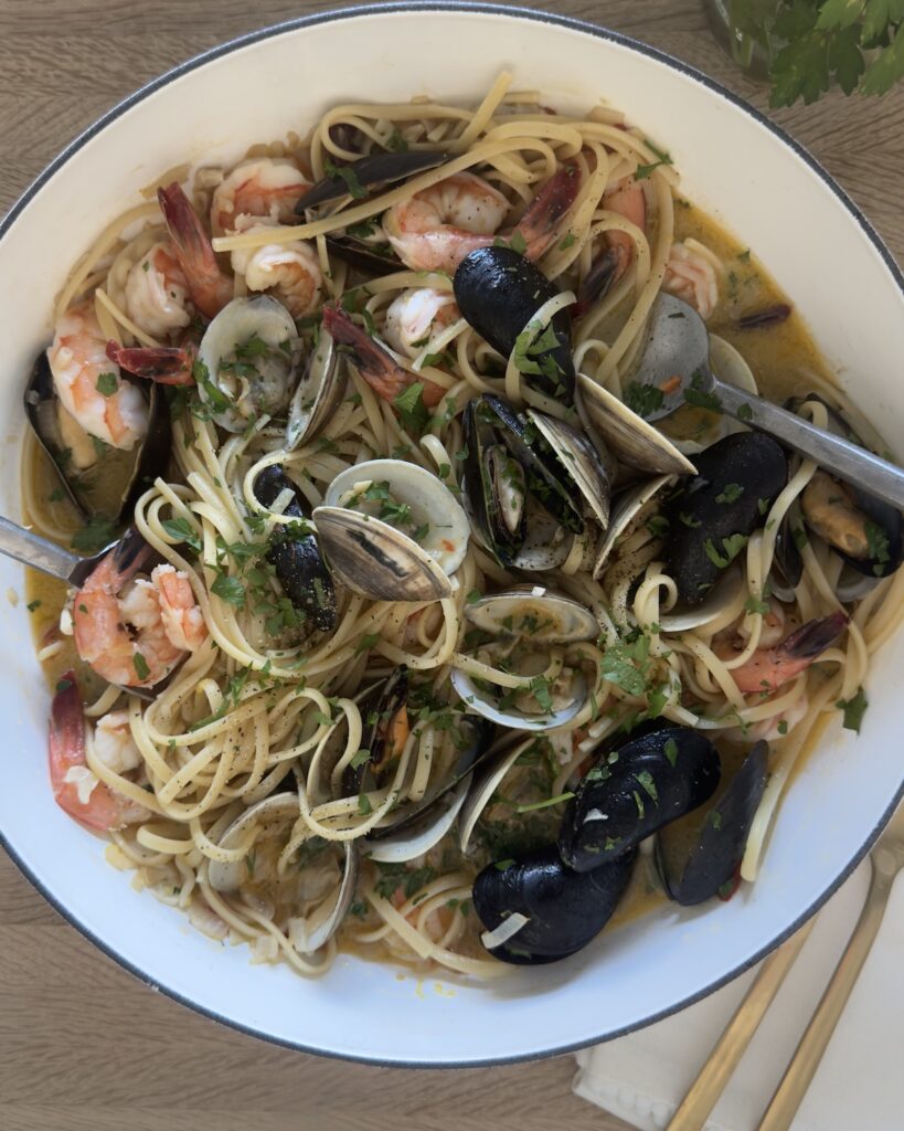 Seafood linguine with clams, mussels, and shrimp tossed in a white wine garlic sauce, garnished with fresh parsley and served in a large white bowl.