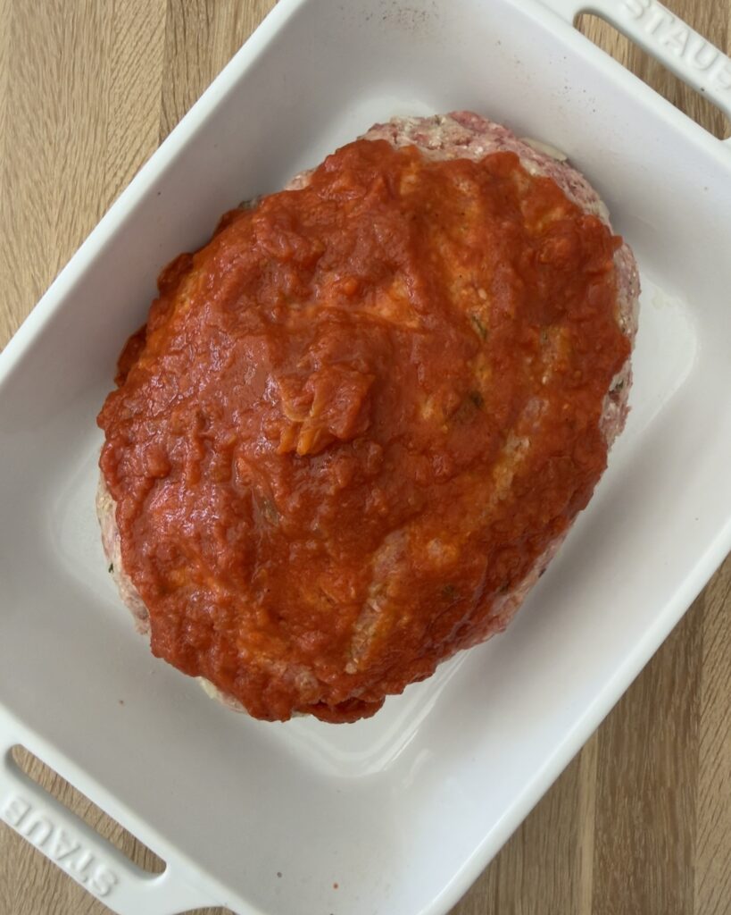 Italian meatloaf in a white baking dish, topped with marinara and ready to be baked in the oven.