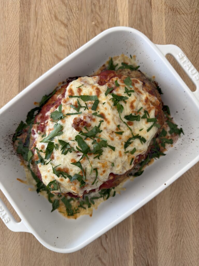 Italian meatloaf topped with melted mozzarella and fresh parsley in a white baking dish