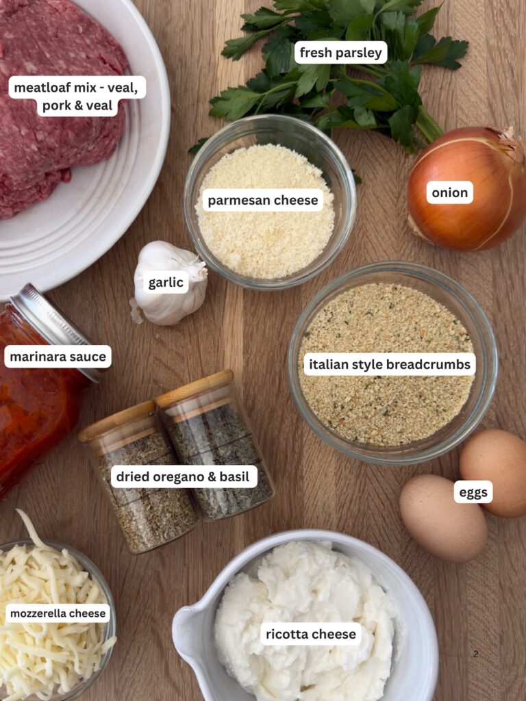 Ingredients for Italian meatloaf including ground meat, ricotta cheese, mozzarella, Parmesan, eggs, breadcrumbs, marinara sauce, garlic, onion, and fresh parsley arranged on a wooden surface