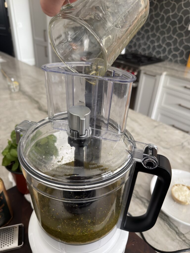 olive oil being streamed into a food processor to make creamy pistachio pesto.