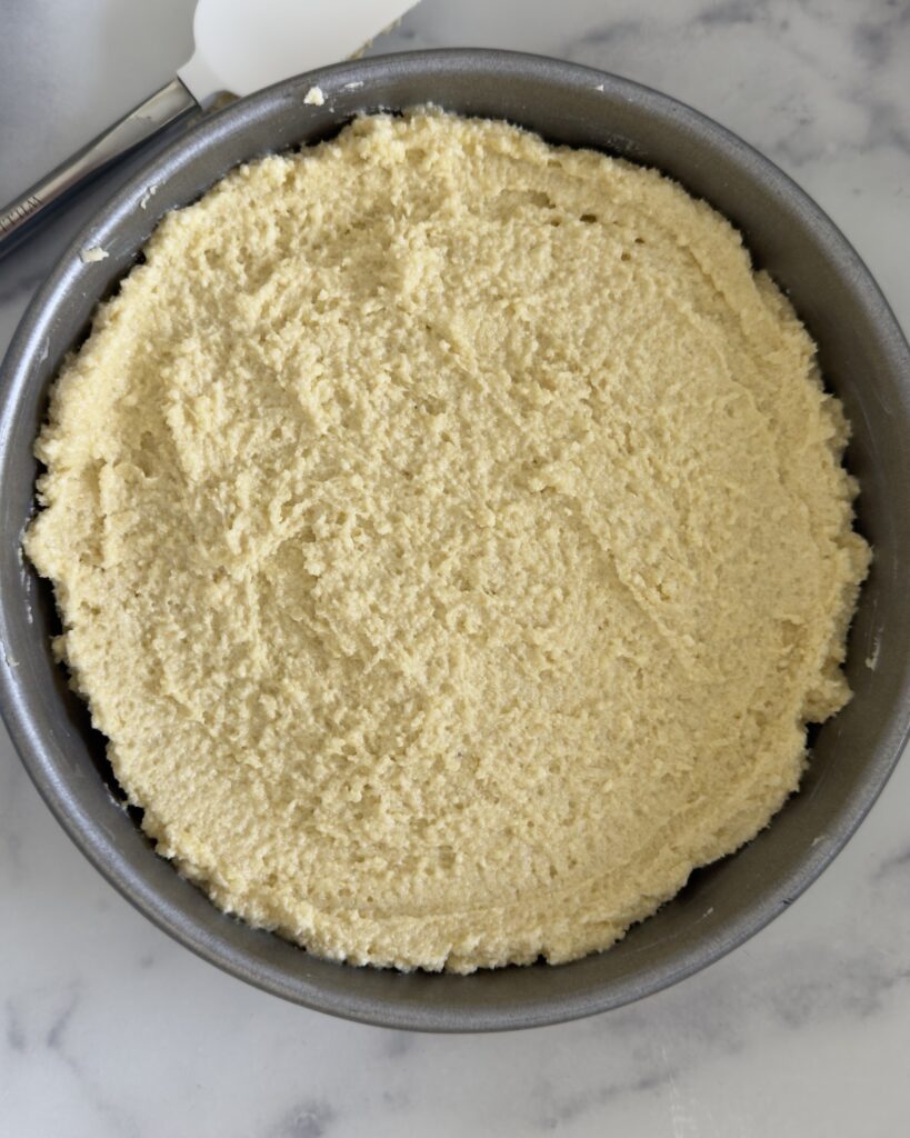Almond ricotta cake batter spread evenly in a parchment-lined round cake pan before baking
