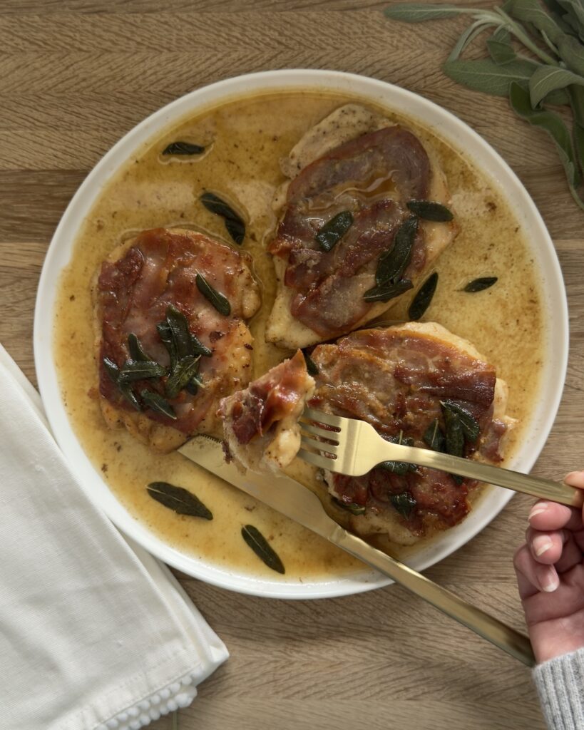 Chicken saltimbocca with prosciutto and sage in a white wine butter sauce, served with a fork cutting into the chicken