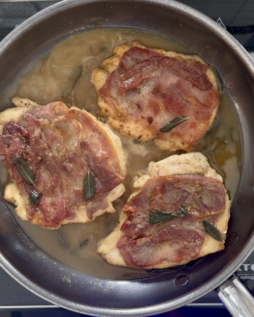 Chicken saltimbocca cooking in a skillet with prosciutto and sage as the chicken sears in a white wine butter sauce