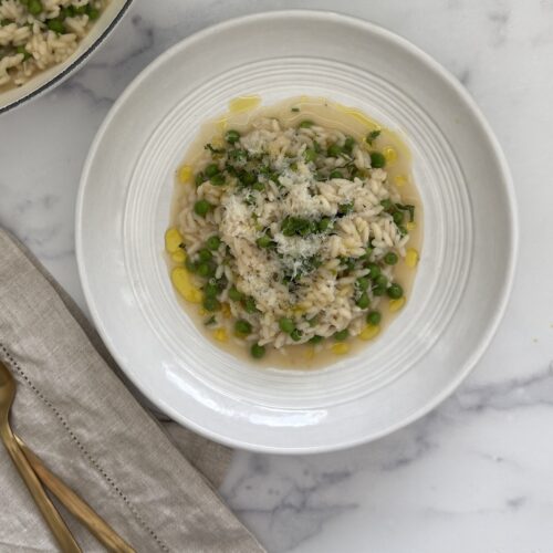 Spring pea risotto with Parmesan cheese, lemon zest, mint, and chives served in a bowl.