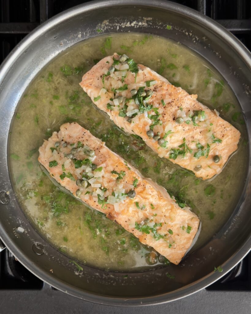 salmon piccata in a skillet with lemon caper sauce and fresh parsley
