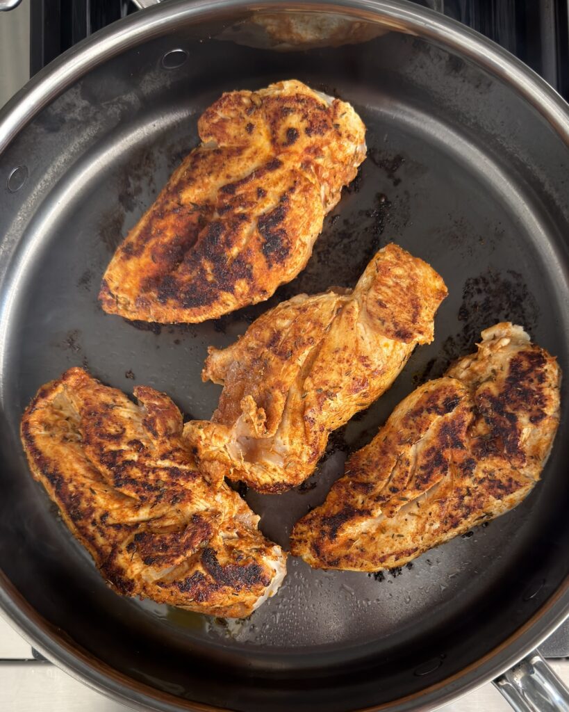 Blackened chicken searing in a skillet with smoky spices and golden crust for creamy blackened chicken fettuccine Alfredo recipe.