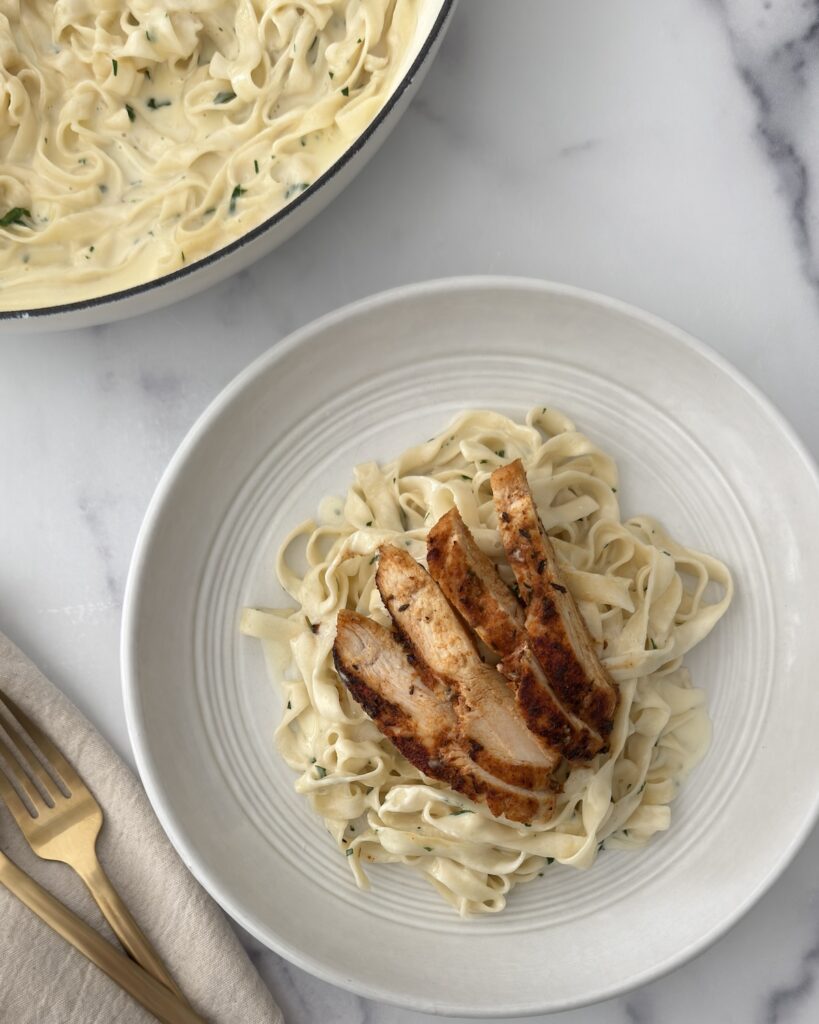 Blackened chicken fettuccine Alfredo with creamy Parmesan pasta and sliced seared chicken served in a white bowl