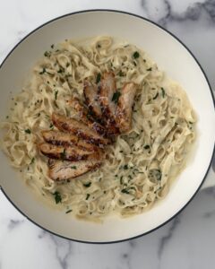 Creamy blackened chicken fettuccine Alfredo with sliced seasoned chicken, Parmesan sauce, and fresh parsley served in a white braiser.