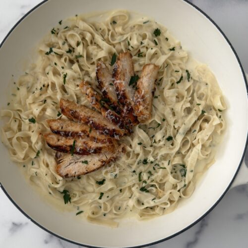 Creamy blackened chicken fettuccine Alfredo with sliced seasoned chicken, Parmesan sauce, and fresh parsley served in a white braiser.