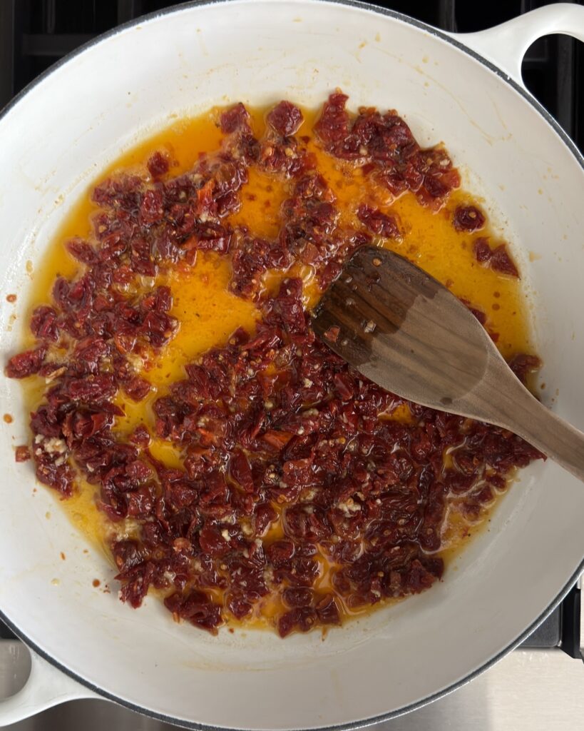 Sun-dried tomatoes cooking in oil in a white braiser for creamy tortellini sauce