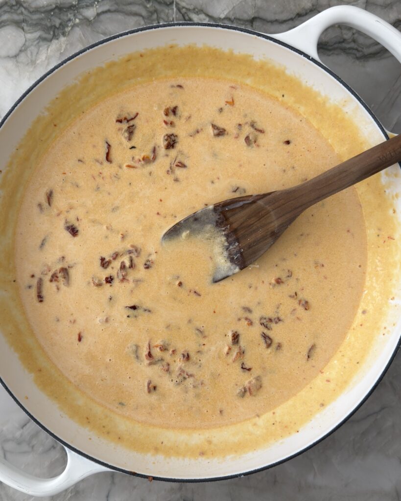 Creamy sun-dried tomato sauce with Parmesan in a white braiser before adding tortellini