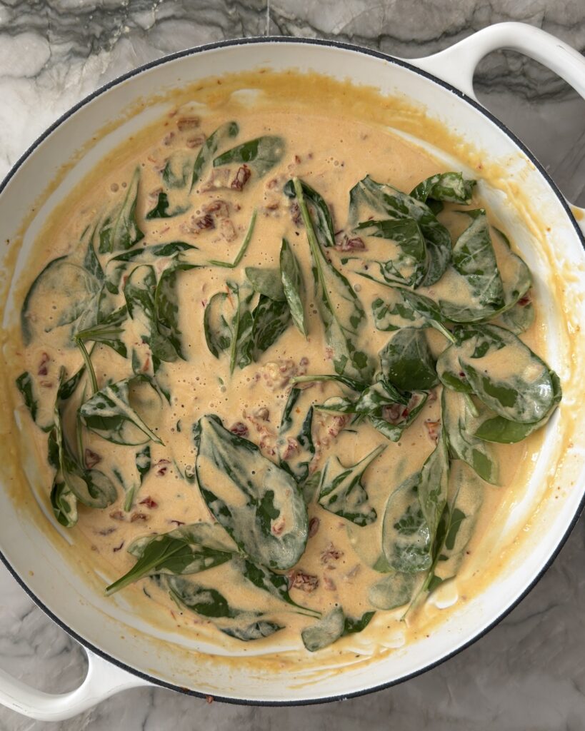 Creamy sun-dried tomato sauce with spinach in a white braiser before adding tortellini.