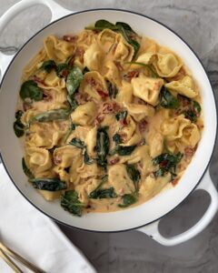 Creamy sun-dried tomato tortellini with spinach and Parmesan in a white braiser