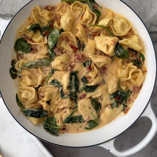 Creamy sun-dried tomato tortellini with spinach and Parmesan in a white braiser