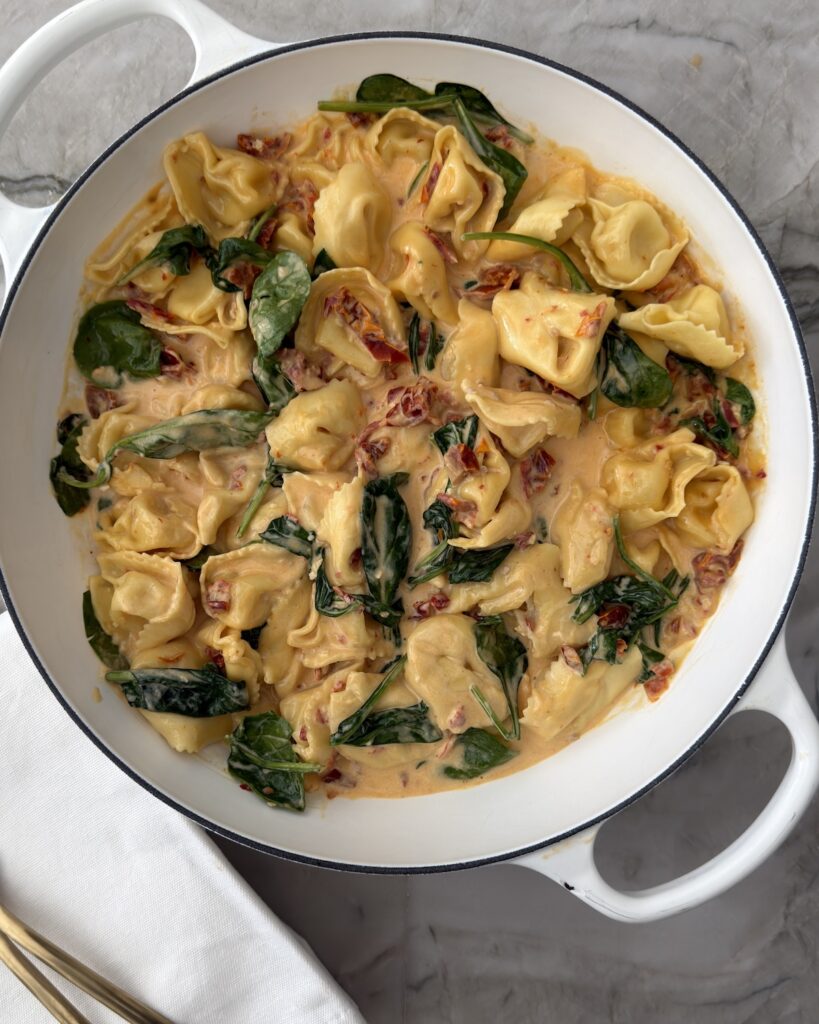 Creamy sun-dried tomato tortellini with spinach and Parmesan in a white braiser