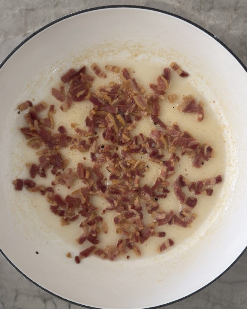 Pancetta crisping in a white skillet for pasta e piselli recipe preparation.