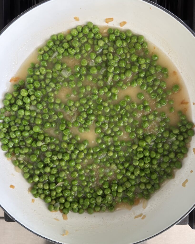 Green peas simmering in pancetta fat and pasta water for pasta e piselli before adding the cooked ditalini pasta.