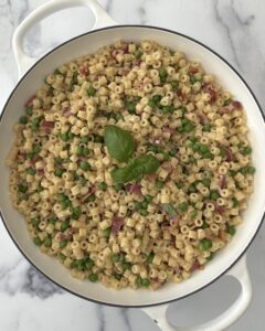Creamy pasta e piselli with ditalini, sweet peas, crispy pancetta, and fresh basil served in a white skillet.