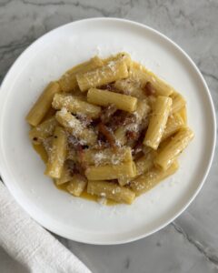 rigatoni carbonara with pancetta and Pecorino Romano cheese served on a white plate
