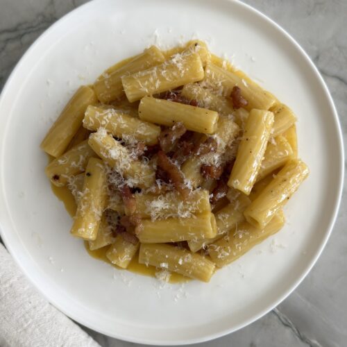 rigatoni carbonara with pancetta and Pecorino Romano cheese served on a white plate