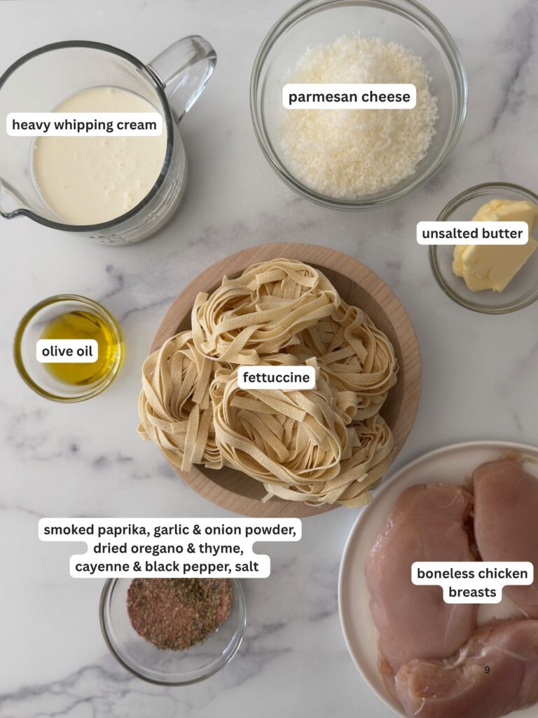Ingredients for blackened chicken Alfredo with chicken breasts, fresh fettuccine, heavy whipping cream, Parmesan cheese, butter, olive oil, and blackened seasoning on a marble countertop.