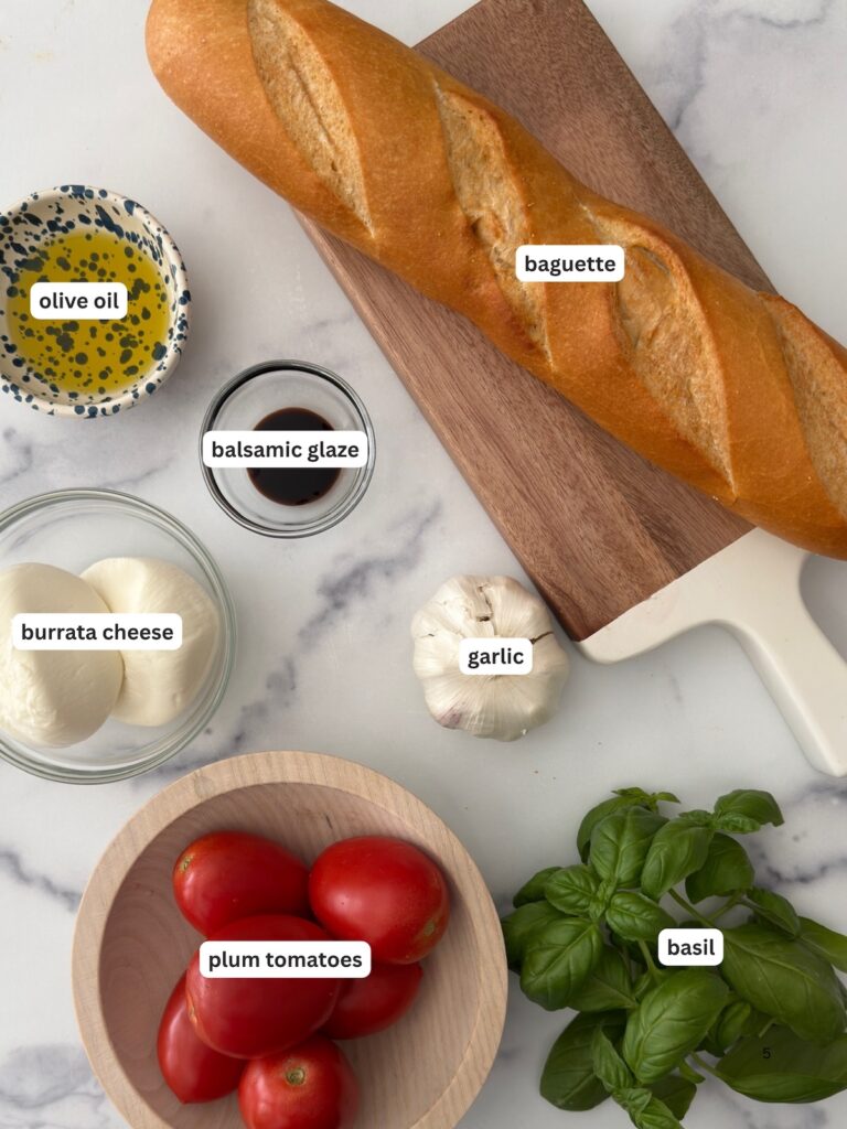 Ingredients for burrata bruschetta including baguette, burrata cheese, tomatoes, basil, garlic, olive oil, and balsamic glaze