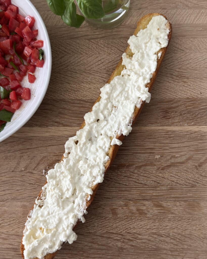 Burrata spread on toasted baguette ready for the tomato basil topping.