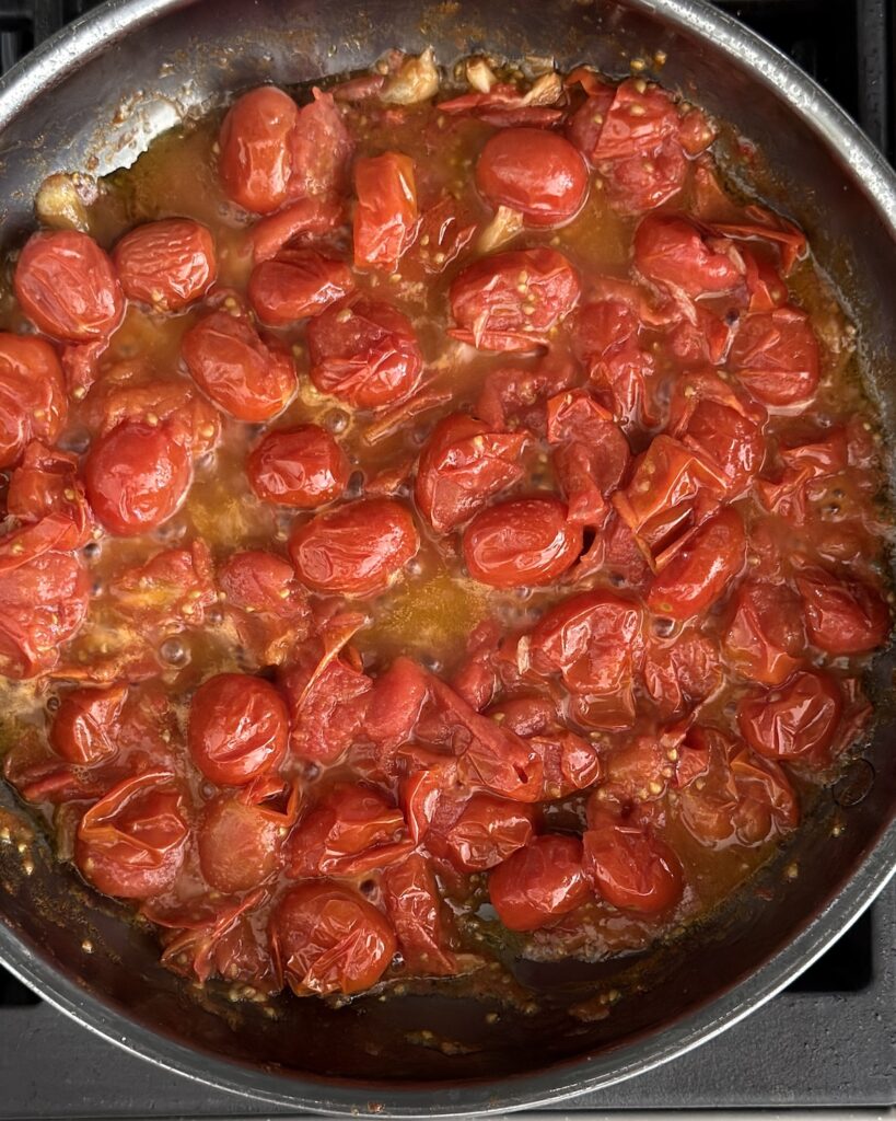Cherry tomato spaghetti sauce simmering in a skillet with blistered cherry tomatoes, garlic, olive oil, and glossy fresh tomato sauce.