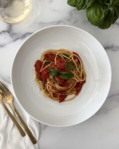 Cherry tomato spaghetti sauce served in a white bowl with blistered cherry tomatoes, spaghetti, fresh basil, and olive oil on a marble surface.