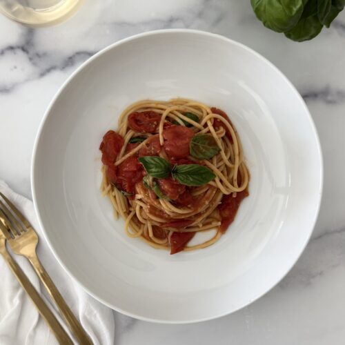 Cherry tomato spaghetti sauce served in a white bowl with blistered cherry tomatoes, spaghetti, fresh basil, and olive oil on a marble surface.