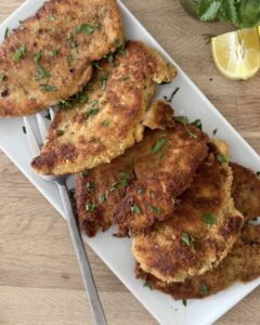 Crispy Italian chicken cutlets on a serving platter with fresh parsley and lemon wedges ready to serve