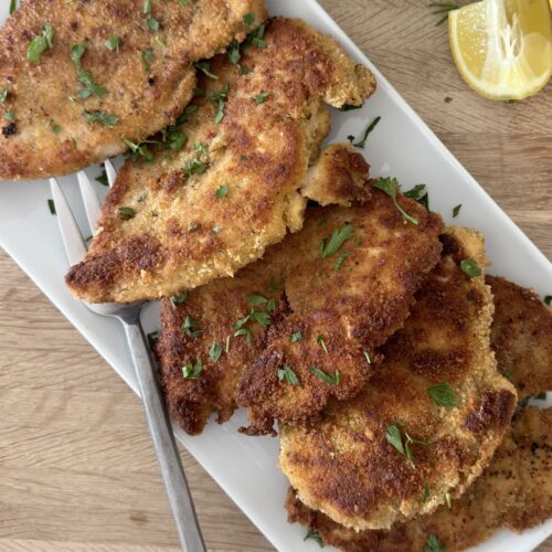 Crispy Italian chicken cutlets on a serving platter with fresh parsley and lemon wedges ready to serve