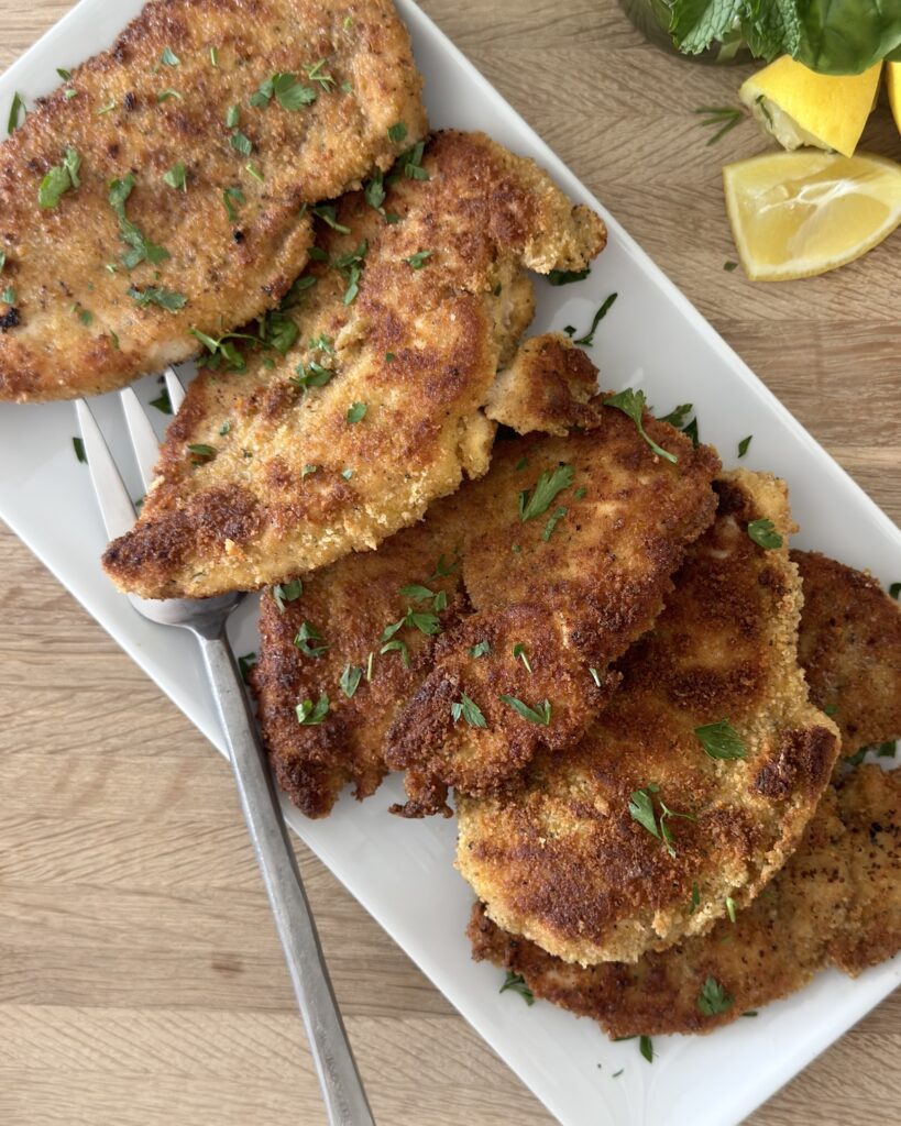 Crispy Italian chicken cutlets on a serving platter with fresh parsley and lemon wedges ready to serve.